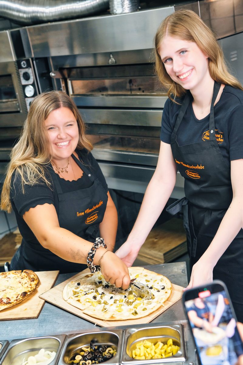 Zwei Mitarbeitende belegen gemeinsam einen Flammkuchen an der Belegstation