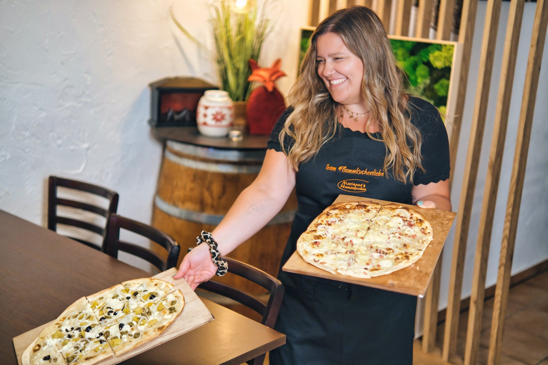 Ein Teammitglied serviert zwei Flammkuchen an einen Tisch im Gastraum